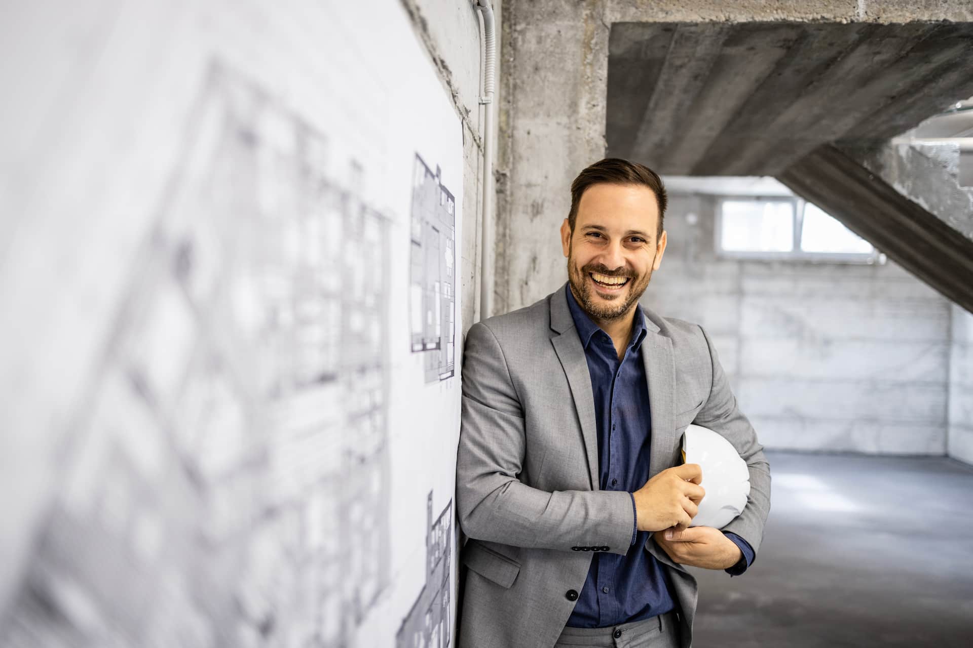 guapo-arquitecto-caucasico-de-pie-junto-al-plan-del-proyecto-en-el-sitio-de-construccion-y-sonriendo-la-camara (1)